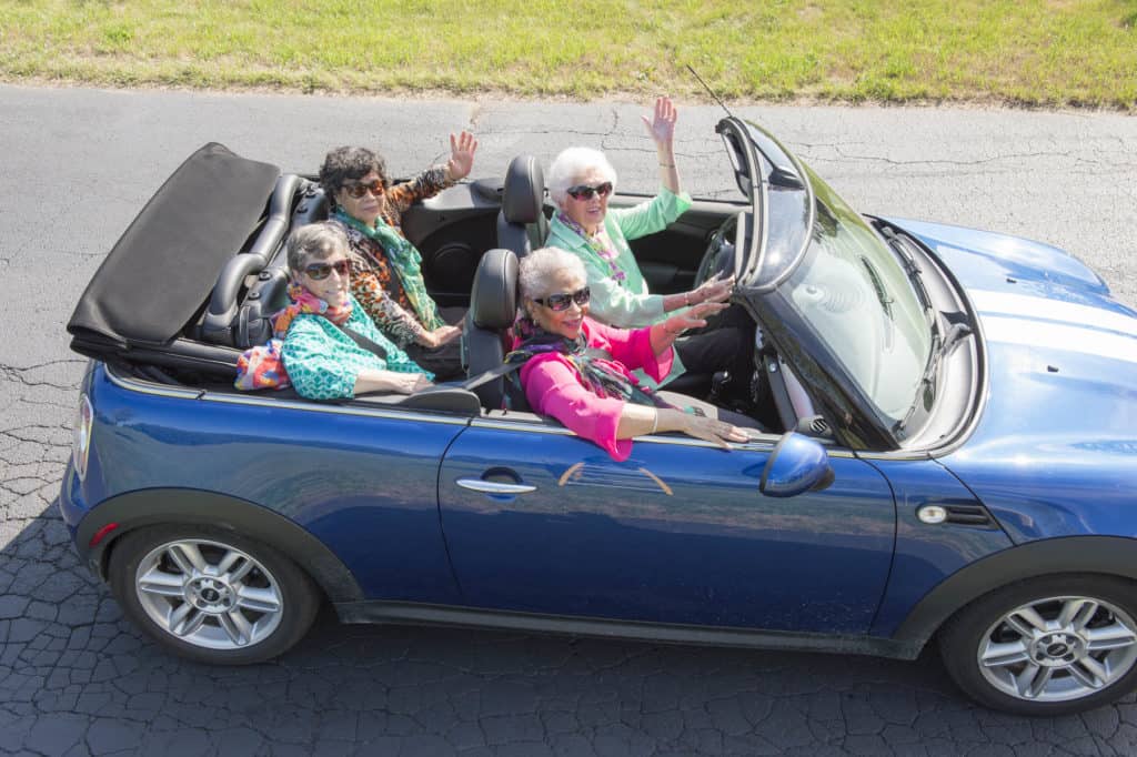 Four seniors waving out of a car