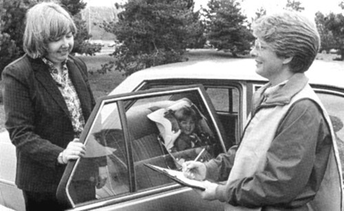 Two researchers outside of vehicle with child in child safety seat.