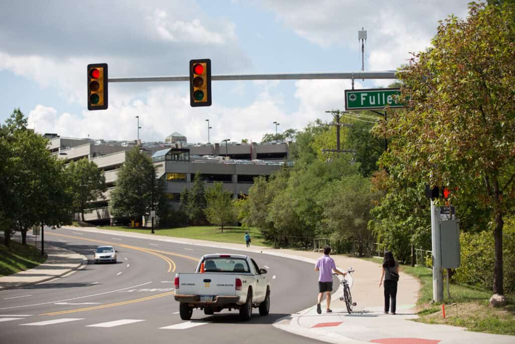 Intersection with red light, truck driving and two pedestrians walking while carrying a bike